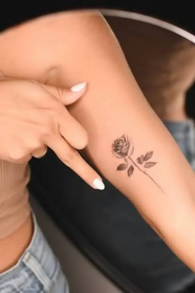 small rose tattoo with soft black and grey shading on the inner forearm