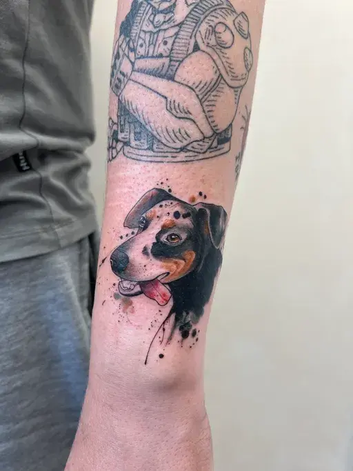  watercolor style dog portrait tattoo with ink splatter on forearm